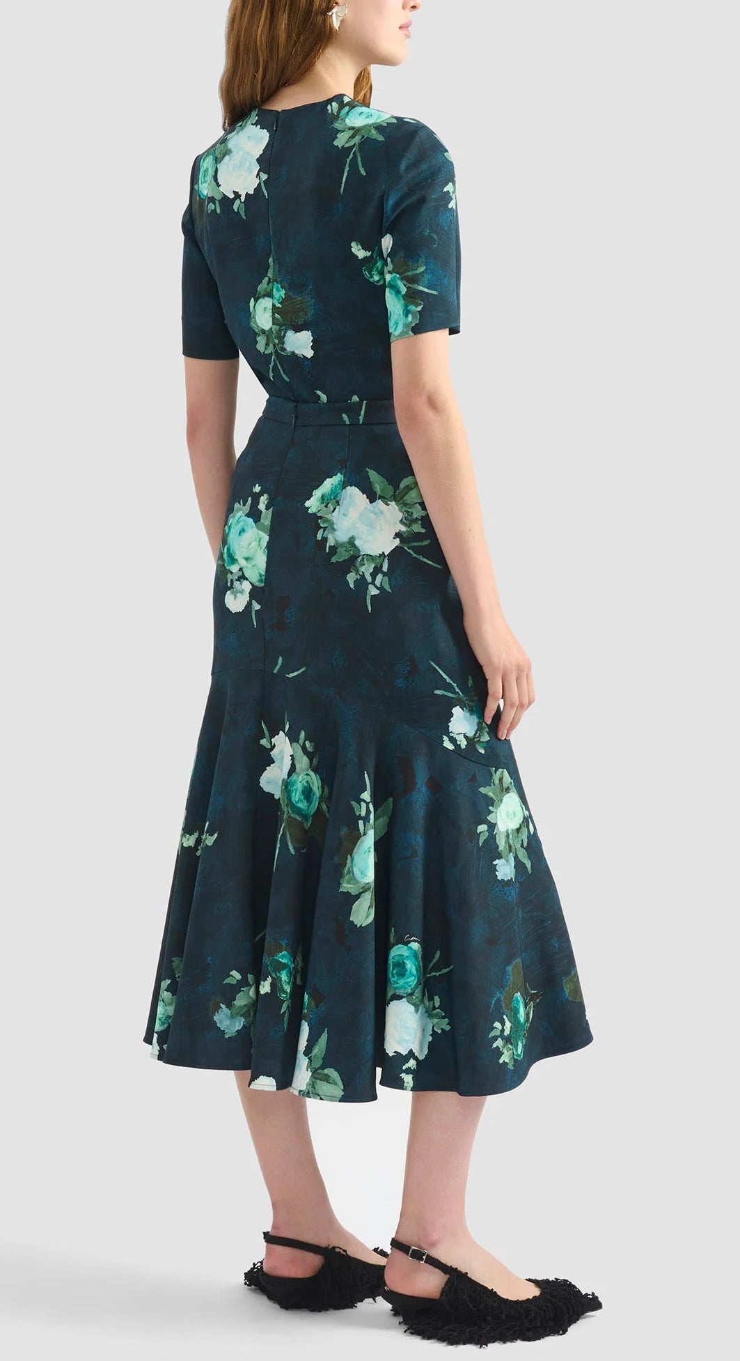 A woman is seen from the back wearing the Erdem Short Sleeve Abstract Rose Top, paired with black textured flat shoes, standing against a plain light background.