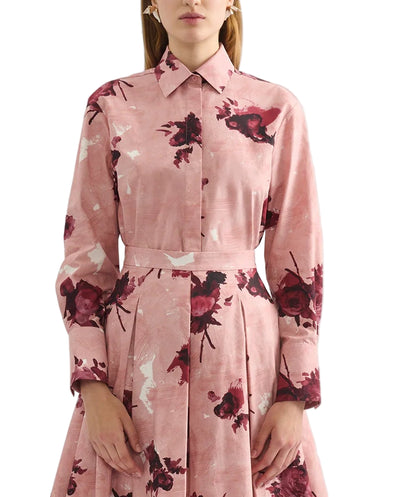 A woman wearing the Erdem Long Sleeve Abstract Rose Shirt, a pink cotton poplin collared dress with dark red floral print and pleated skirt, shown from the waist up.