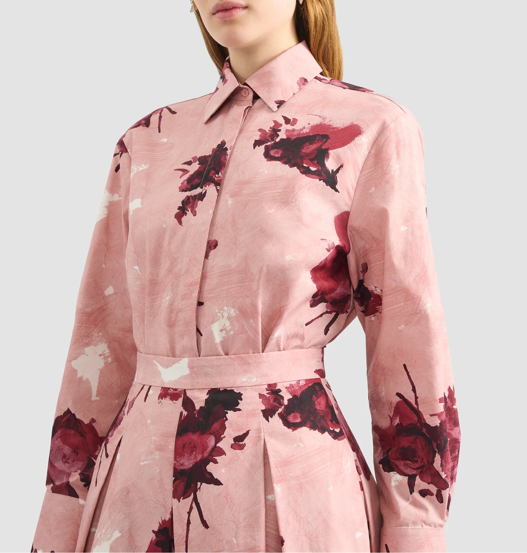A woman wearing Erdem’s Long Sleeve Abstract Rose Shirt, a pink cotton poplin dress with red floral print, is shown from shoulders to waist.
