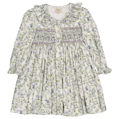 The Kidiwi Adeline Smocked Dress features a long-sleeved design with a ruffled smocked collar and a romantic print, displaying green and purple flowers on a white background.