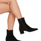 A person displays Staud's chic Aimee Short Boot—black suede ankle booties with mid-height block heels and side zippers—posed elegantly against a pristine white background.