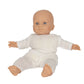 A doll named Alfie by Konges Slojd is dressed in a white, textured one-piece outfit made from organic cotton, sitting with both arms outstretched and legs slightly bent.