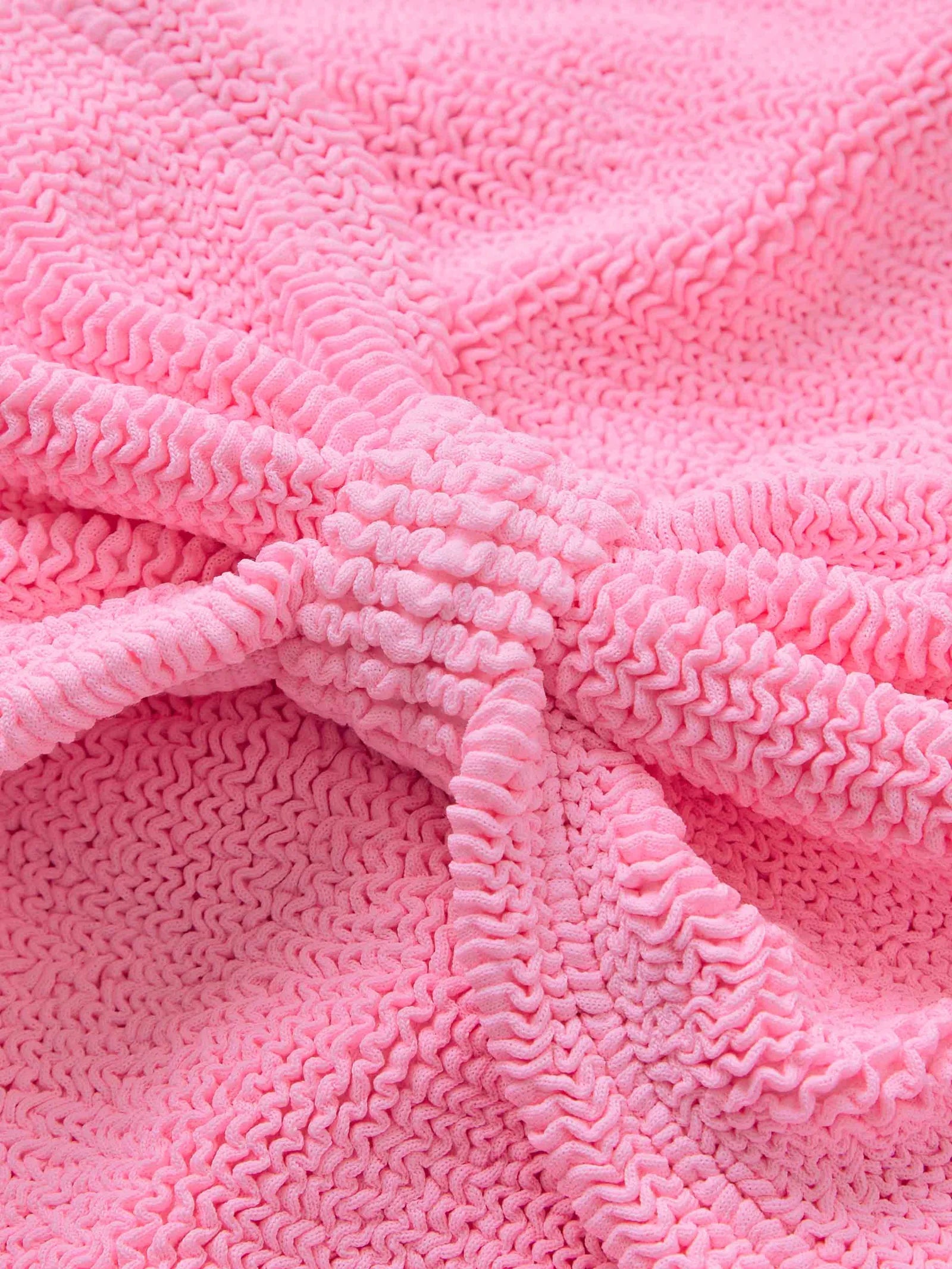 Close-up of the Bonnie Bikini by Hunza G, featuring textured pink ruched fabric with a central gathered knot, evoking classic retro and supportive bikini styles.