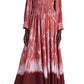 A person wears the Altuzarra Kathleen Dress, a long-sleeved red and white shibori tie-dye dress with an elastic waist, paired with pink high heels, standing gracefully in a studio.