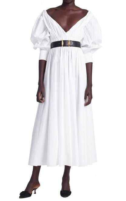 The person is wearing the Altuzarra Kathleen Optic White Dress, featuring a V-neck and puffed sleeves, cinched with a black belt, and paired with sleek black heels.