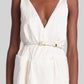 Against a neutral background, someone wears a sleeveless white dress with a deep V-neck, accessorized by Altuzarra's Skinny Belt featuring a gold-tone metal buckle.