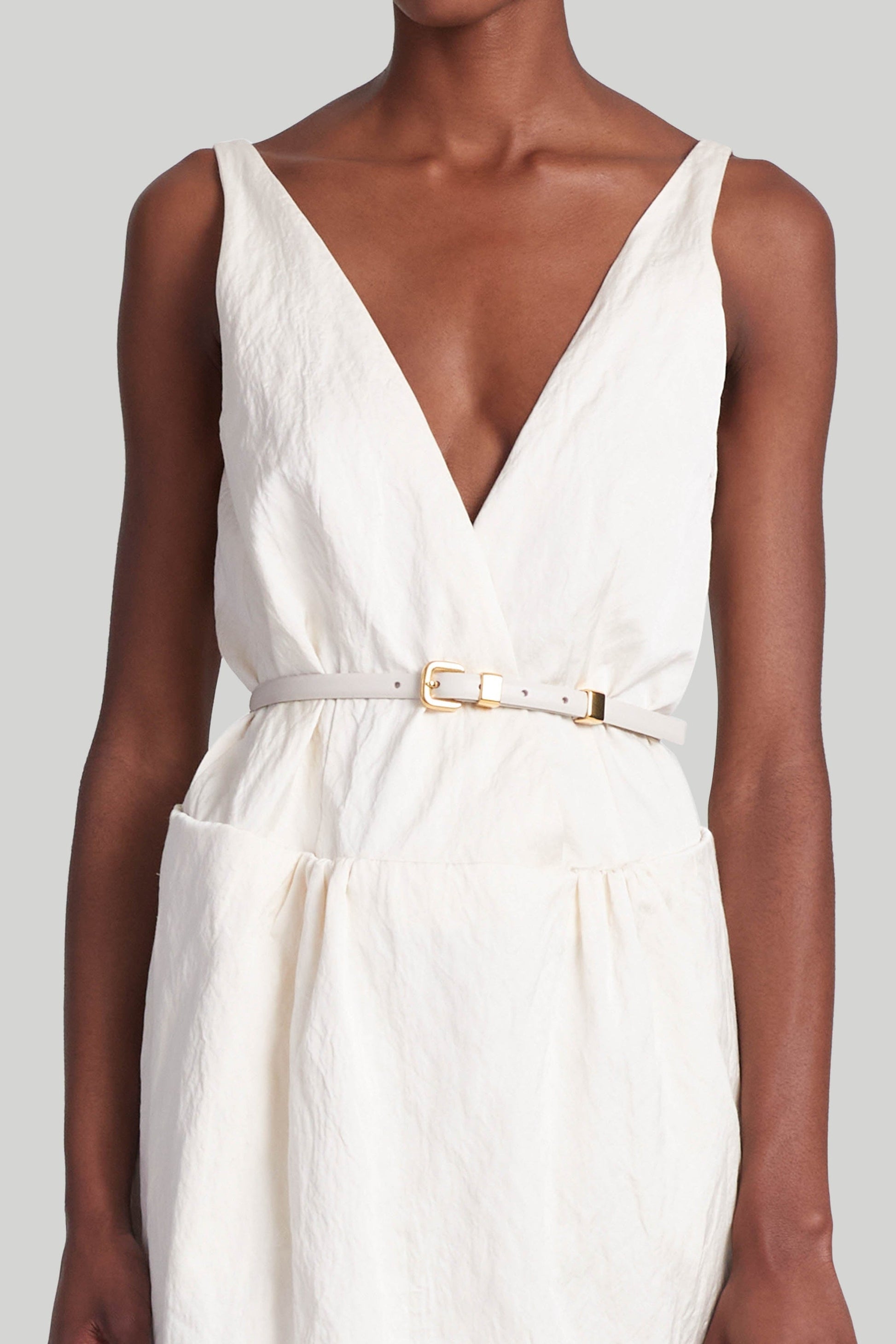 A person wearing a sleeveless, V-neck white dress paired with an elegant Altuzarra Skinny Belt, an exquisite piece crafted in Italy.