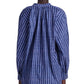 A person is wearing the Altuzarra Teresa Top, a loose-fitting, long-sleeved blue and white striped blouse with balloon sleeves and buttoned cuffs, viewed from the back.