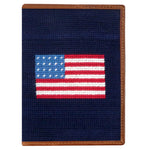 The Smathers & Branson American Flag Passport Case features a small rectangular needlepoint design with an American flag on a dark blue background and fine Italian leather trim—ideal as a travel organizer.