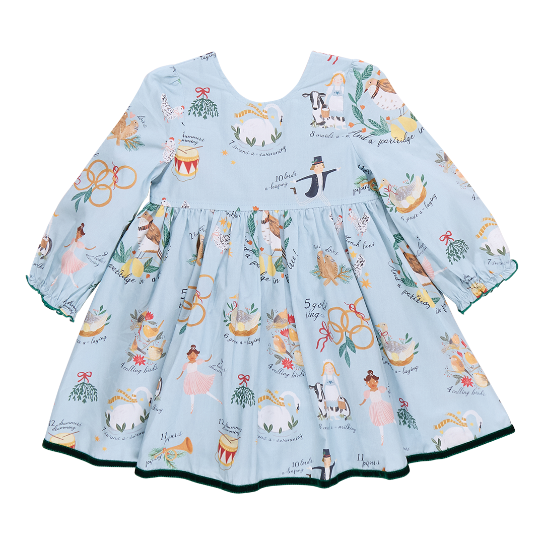 A children's Amma Dress by Pink Chicken, featuring long sleeves and a festive pattern of musicians, floral motifs, and animals inspired by the 12 Days of Christmas, available in blue.