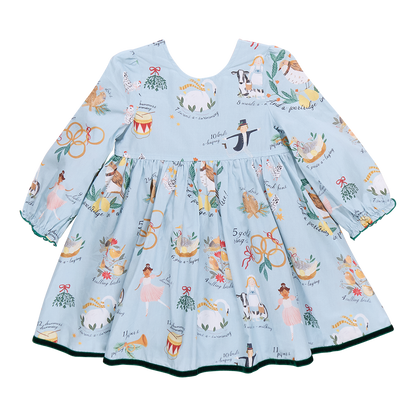 A children's Amma Dress by Pink Chicken, featuring long sleeves and a festive pattern of musicians, floral motifs, and animals inspired by the 12 Days of Christmas, available in blue.