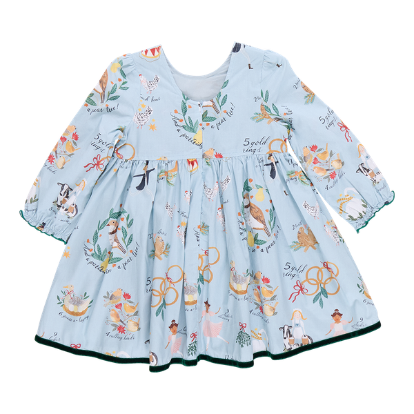 The Pink Chicken Girls Amma Dress is an enchanting light blue long-sleeve outfit, decorated with charming holiday-themed prints inspired by the 12 Days of Christmas, showcasing wreaths, birds, and musical instruments.