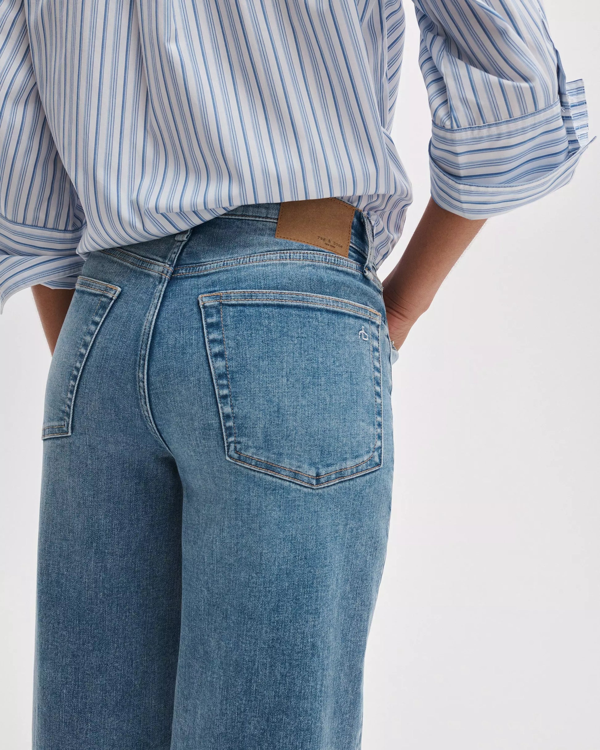 Model wearing Rag & Bone Flexi Andi Full Wide high-waisted, wide-leg light blue denim jeans, paired with a blue and white striped shirt. Shown from the waist down with hands in back pockets.