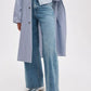 A person wearing Rag & Bone's Flexi Andi Full Wide high-waisted, wide leg jeans, a blue and white striped shirt with a matching long coat, and silver ballet flats stands against a plain background.