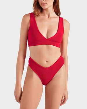 A woman wears the Hunza G Angel Bikini, featuring a textured red V-neck top and high-waisted bottoms, standing against a plain light background.