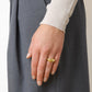 A person's left hand rests on a grey garment, displaying the Lie Studio Anna Ring—a thick, 18k gold-plated stackable piece—on the ring finger, with neatly manicured nails.