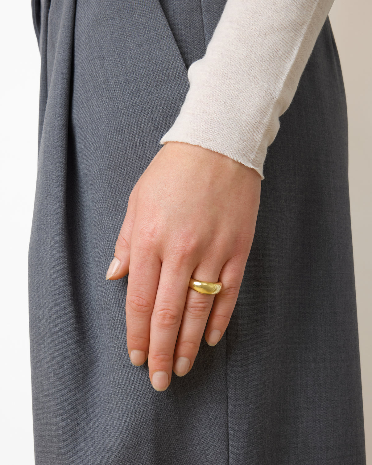 A person's left hand rests on a grey garment, displaying the Lie Studio Anna Ring—a thick, 18k gold-plated stackable piece—on the ring finger, with neatly manicured nails.