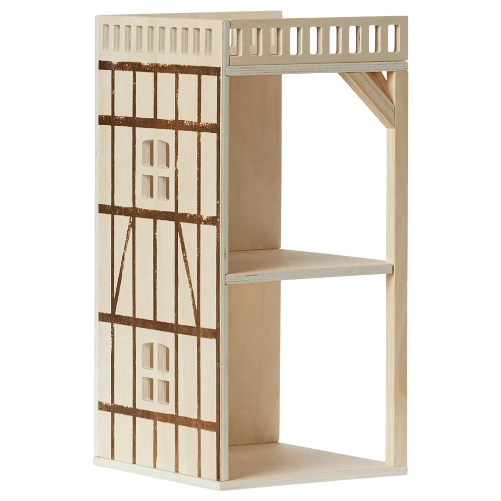 Maileg's Mouse Hole Farmhouse - Annex is a wooden open-back dollhouse showcasing a white and brown half-timbered design, complete with two floors and a balcony railing on the top floor.