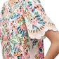 A person wearing the Figue April Dress, a colorful floral piece with flutter sleeves, scallop embroidery, and eyelet lace details.