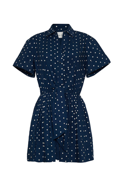 The Cara Cara Asbury Dots Mini Dress features white polka dots on navy, a collared neckline, button front, and self-tie waist sash—an effortlessly stylish sell-out favorite.