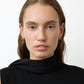 A woman with light skin and long brown hair wears a black sleeveless top and Lie Studio Asta Earrings, facing forward against a plain white background.