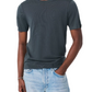 A person wearing the Rag & Bone Aulton Knit Tee, a dark fine jersey crewneck, paired with light blue jeans and one hand in their pocket, stands against a plain white background.