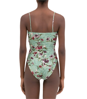 Someone wears the Durazno Embroidered One Piece by Agua By Aguabendita, a green floral swimsuit with thin shoulder straps and a low-cut back, crafted from grecycled polyester and shown from behind.