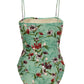 The Durazno One Piece by Agua By Aguabendita is a teal swimsuit with thin straps, crafted from recycled polyester and adorned with a multicolored floral print. It features built-in UPF 50 sun protection for stylish comfort on sunny days.