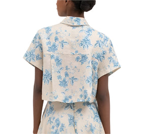 A person is seen from the back, wearing an Agua by Aguabendita Virtuosa Cropped Shirt, a light-colored short-sleeved floral button-down with a collar, and a matching skirt in the Bougainvillea design.