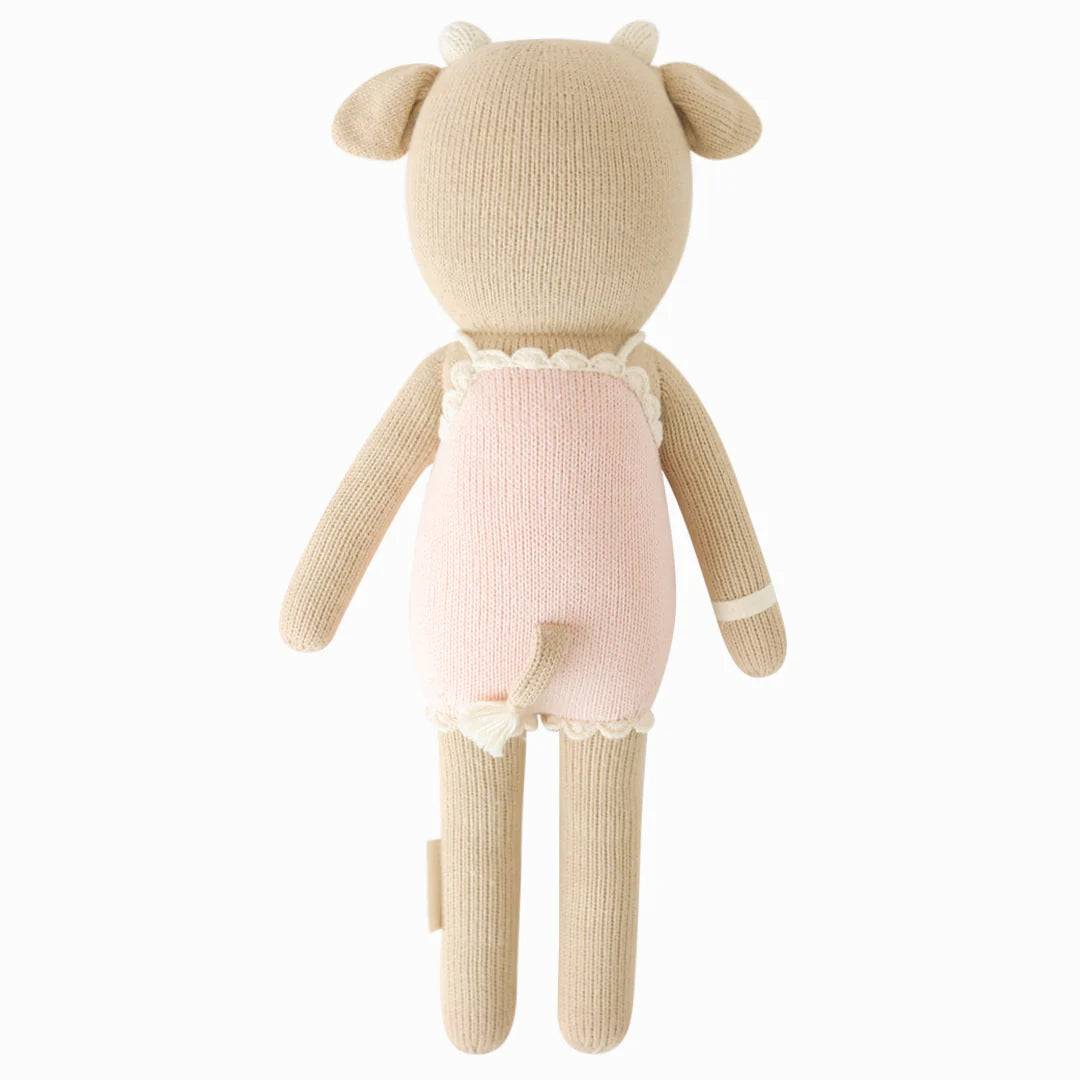 Ava the Cow Powder Pink by Cuddle + Kind is a 20" knitted plush toy featuring cute horns, ears, and a tail in a powder pink outfit with cream trim—perfect for birthday cuddles or playtime in a sweet berry meadow.