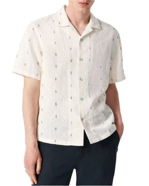 A person wears the Avery Embroidered Camp Shirt by Rag & Bone—a short-sleeve, off-white cotton-linen blend with a subtle pattern—paired with black pants for the perfect summer look.