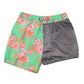 The Snapper Rock Coastal Shells Swim Shorts for kids feature a two-tone design: floral pattern on green on the left and solid gray on the right, with an elastic waistband and adjustable drawcord for a perfect fit.