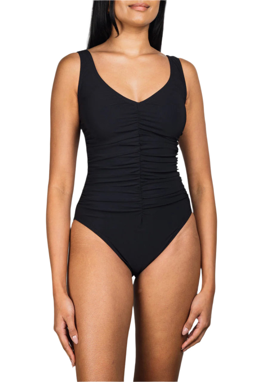 A woman models the Karla Colletto Basics V-Neck Tank with High Back One Piece, a black swimsuit featuring wide straps and center-front ruching for a flattering, shape-enhancing fit, set against a white background.