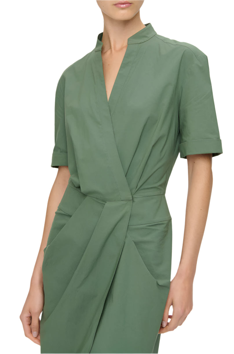 A person wearing the Bali Dress by Callas Milano, a green knee-length wrap dress with short sleeves and pocket details, crafted from ethically sourced cotton.