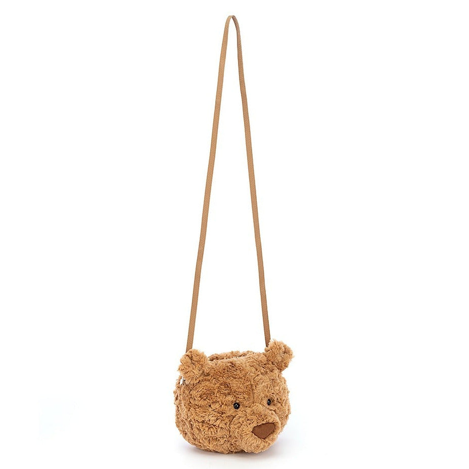 The Jellycat Bartholomew Bear Bag is a small brown cross-body bag with a long strap, featuring a teddy bear’s face, complete with ears, eyes, and nose.