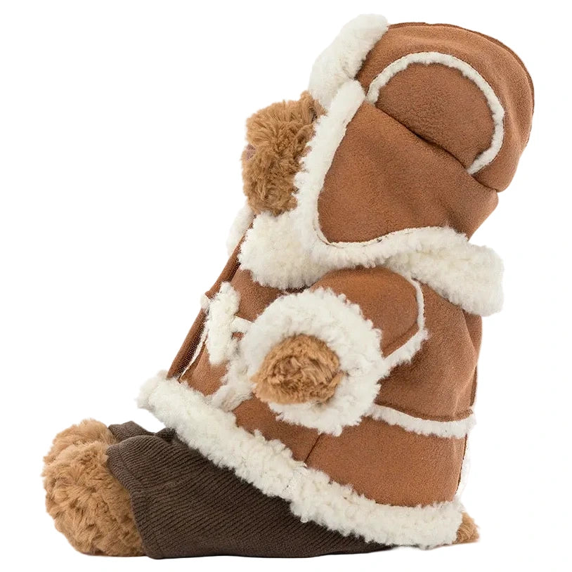 Side view of a Jellycat Bartholomew Bear ‘Alpine’ wearing a hooded, shearling-trimmed winter coat.