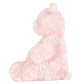A side view of Jellycat's Leola Bear Medium, a pink, fluffy artist bear, sitting upright against a plain white background in a South London studio.
