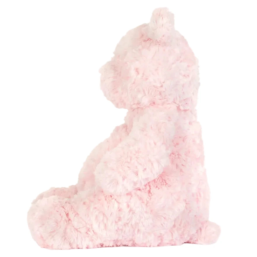 A side view of Jellycat's Leola Bear Medium, a pink, fluffy artist bear, sitting upright against a plain white background in a South London studio.