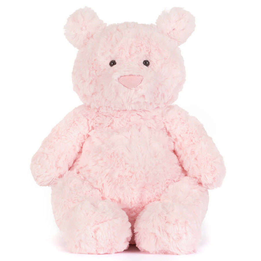 The Jellycat Leola Bear Medium is a light pink plush bear with a round body, floppy arms and legs, and small black eyes. It sits upright on a plain white background, handcrafted in a South London studio.