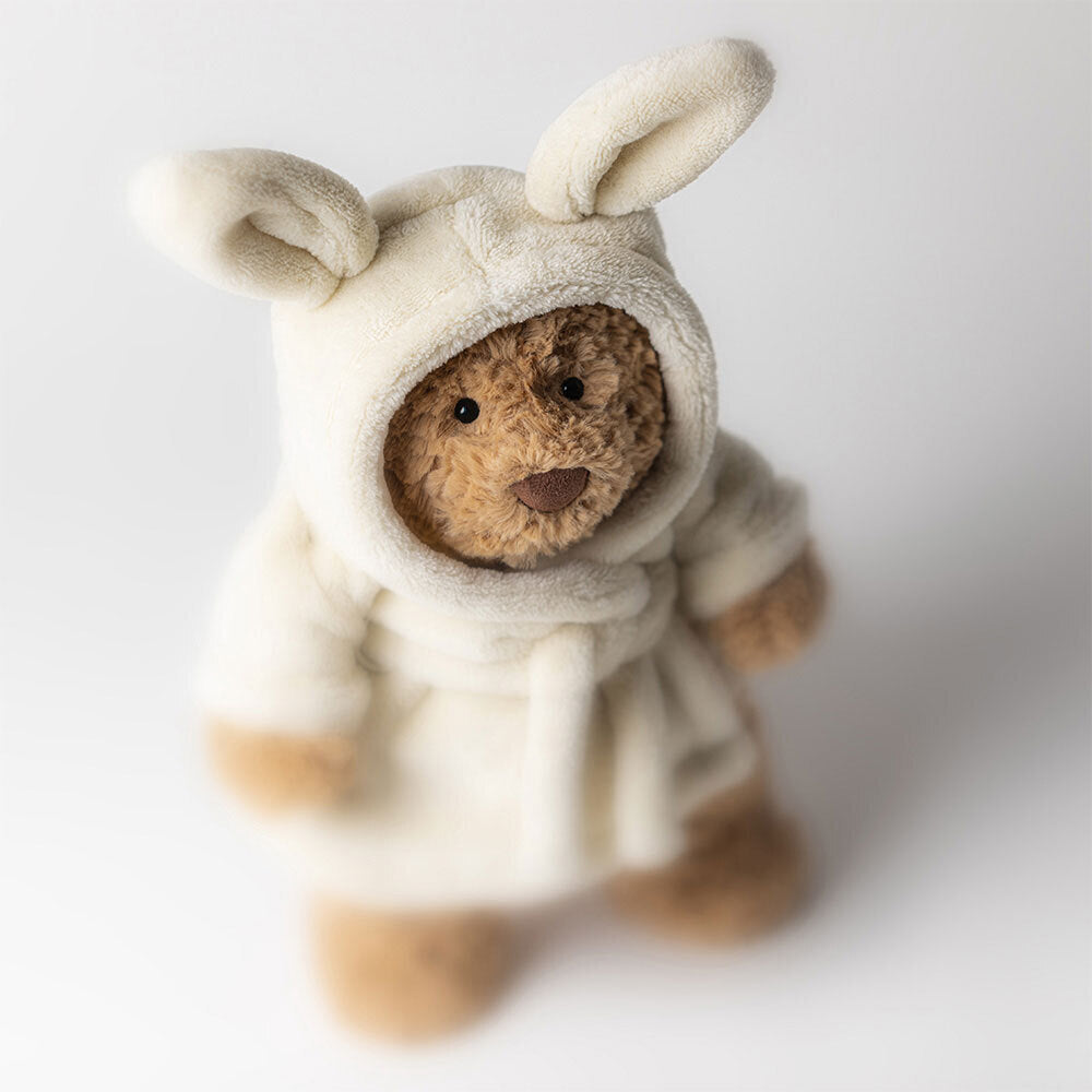 Bartholomew Bear Bathrobe by Jellycat is a plush bear dressed in a soft, white hooded robe with bunny ears, shown on a light background.