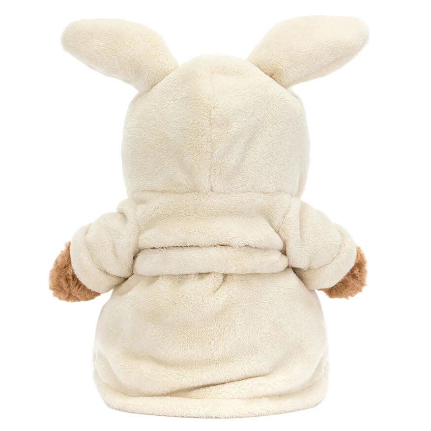 The Jellycat Bartholomew Bear Bathrobe is a stuffed bear dressed in a cream hooded robe with bunny ears, shown from the back.