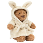 Bartholomew Bear Bathrobe by Jellycat sits upright, wearing a cream hooded robe with bunny ears and a tied belt—this adorable plush bear is perfect for cozy hugs.
