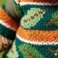 Close-up of a knitted sweater with green, orange, white, and brown zigzag stripes—perfect for pairing with your Jellycat Bartholomew Bear Hiking Outfit.