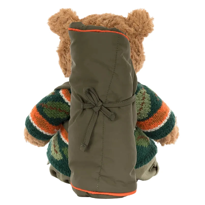 The Jellycat Bartholomew Bear Hiking Outfit shows Bartholomew Bear in a patterned sweater with an olive green sleeping bag on his back, viewed from behind.