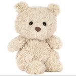 A Bartholomew Bear Junior teddy bear from Jellycat, featuring beige fluffy fur, black eyes, and a brown nose, sits upright against a white background.