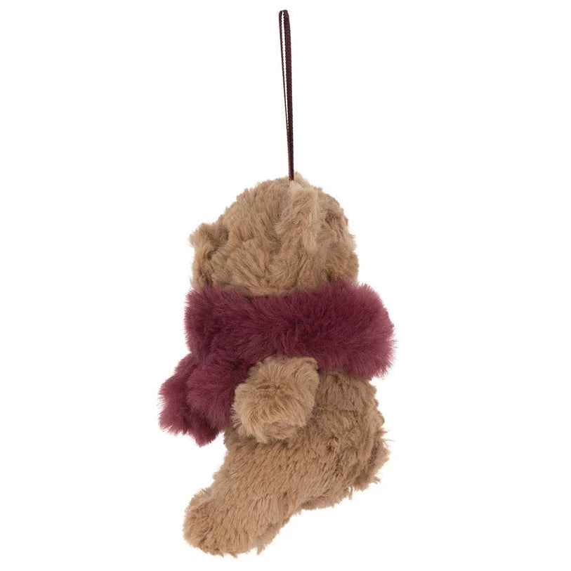 A brown Jellycat Bartholomew Bear Winter Warmer Decoration plush ornament wearing a deep red scarf, hanging by a string.