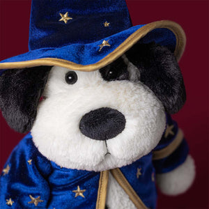 Jellycat’s Rufferty Puppy Wizard Outfit plush dog toy, dressed in a blue wizard costume adorned with yellow stars and complete with a wide-brimmed hat and robe, appears against a dark red background.