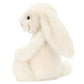 The Jellycat Bashful Bunny Cream Medium sits upright, facing left, with long floppy ears and ultra-soft fur—an ideal cuddly companion for lazy summer days.