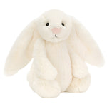 The Jellycat Bashful Bunny Cream Medium, with long floppy ears, black eyes, and a pink nose, sits upright against a white background—perfect for cuddling on relaxed summer days.