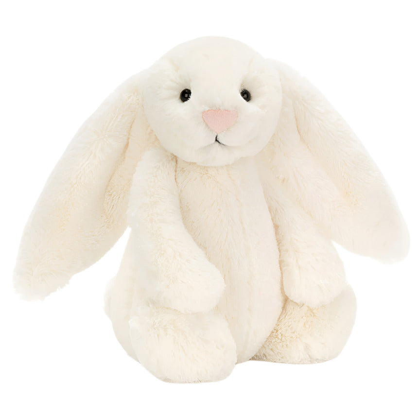 The Jellycat Bashful Bunny Cream Medium, with long floppy ears, black eyes, and a pink nose, sits upright against a white background—perfect for cuddling on relaxed summer days.